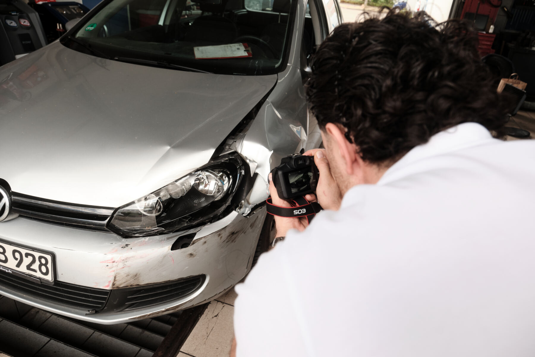 Ein Gutachter fotografiert den Unfallschaden an der Front eines silbernen Autos in einer Werkstatt zur Dokumentation.