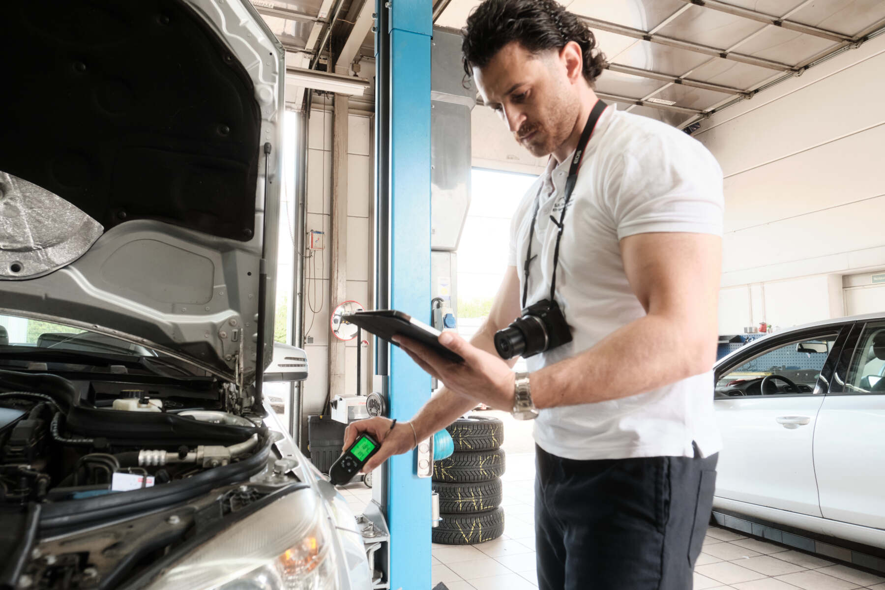 Mechaniker führt eine Kfz-Inspektion durch und prüft den Motorraum mit Diagnosegerät in einer Autowerkstatt.
