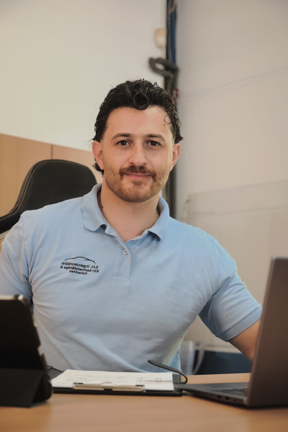 Porträt eines Mitarbeiters im Büro am Schreibtisch, sitzend vor Laptop und Unterlagen.